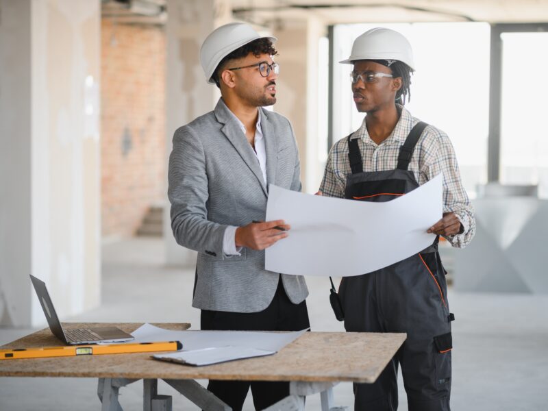 Architect,And,Builder,Discussing,Blueprints,At,A,Construction,Site.,Teamwork